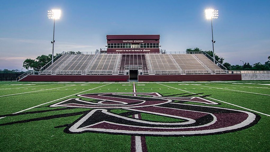 Empty football stadium with stands, field, and "SSU" logo. Two tall lights are on.