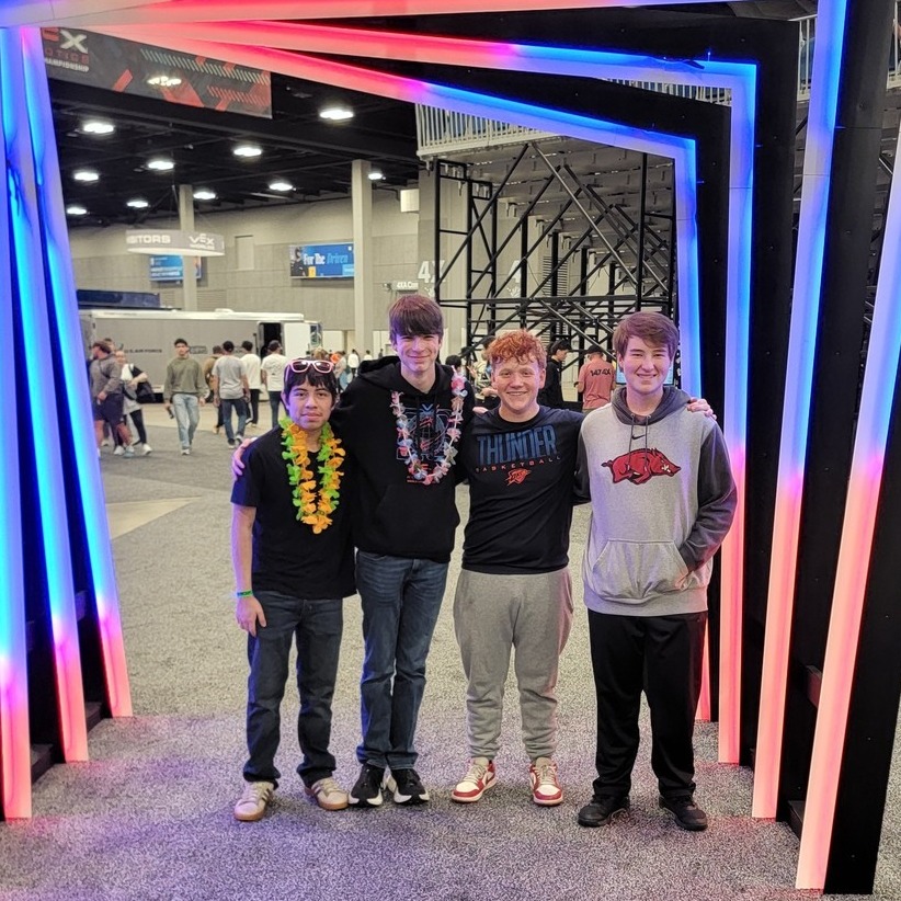 Four people stand under a colorful light installation in a room, smiling and looking at the camera.