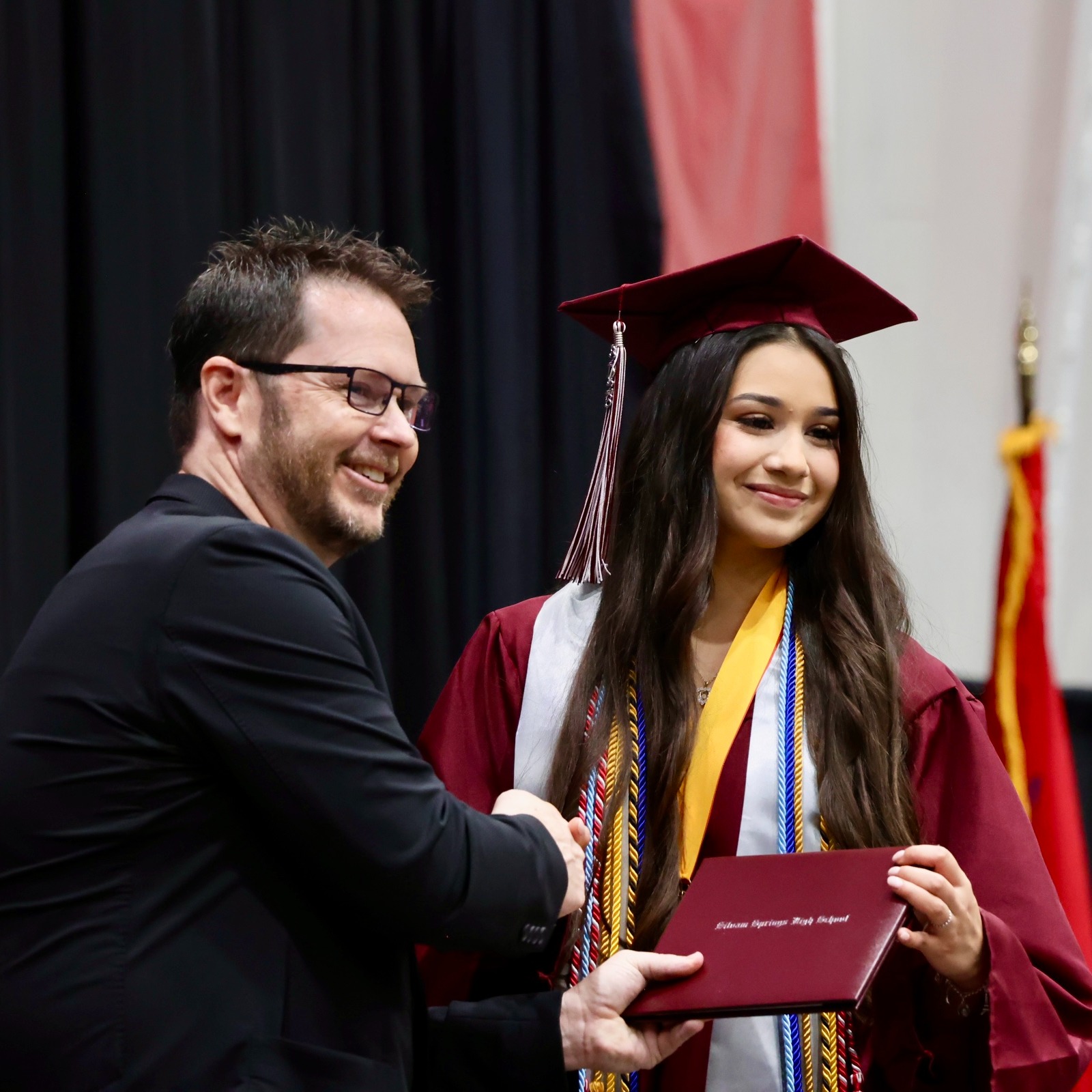 A graduate wearing a cap and gown receives a diploma from a man at a graduation ceremony.