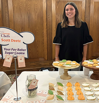 A woman standing behind a table with cookies and other items.