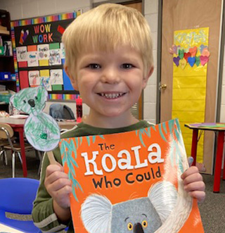 A young boy proudly displaying a book featuring koala bears.