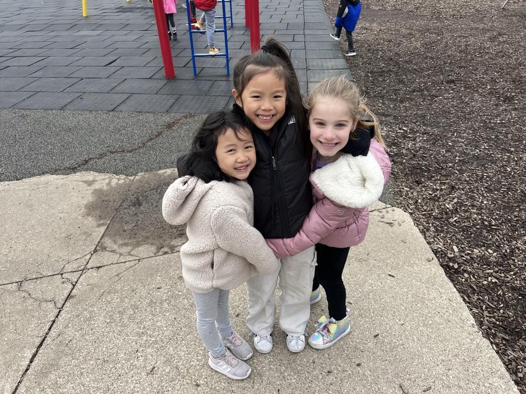 Three children smiling and posing for a photo in a playground area.