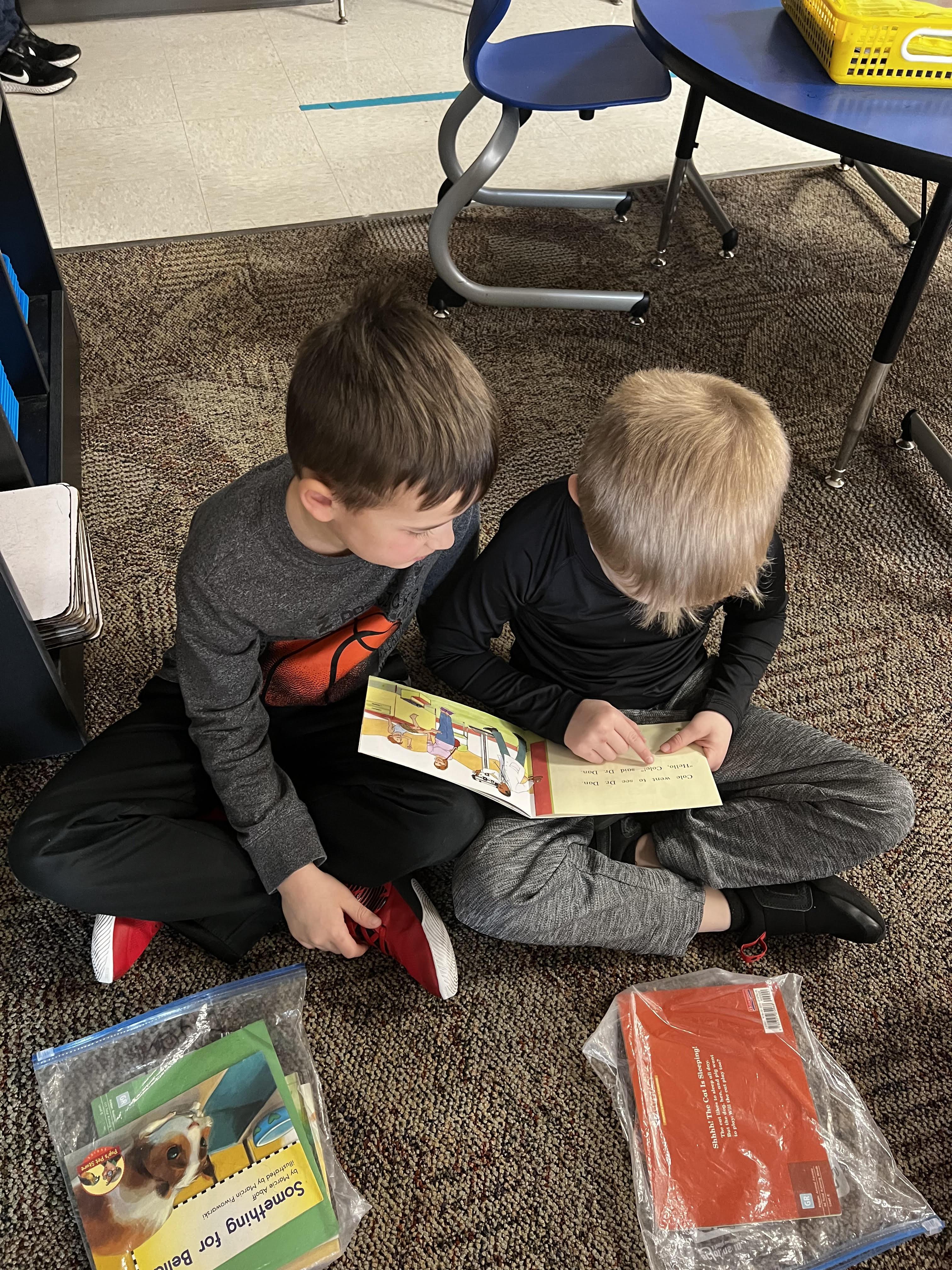A boy and a girl sitting on the floor, engrossed in reading books.