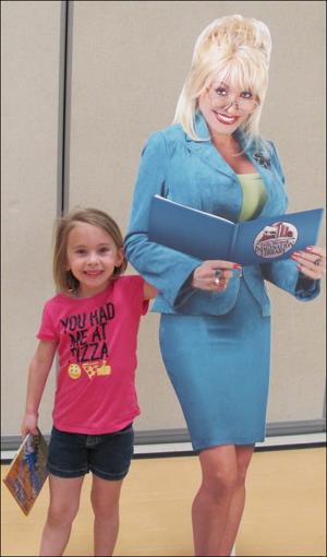 A young girl smiles while standing beside a large, colorful dolly, showcasing her playful spirit and imagination.