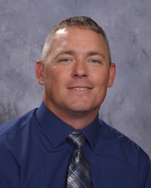 A man in a blue shirt and tie smiling.