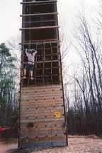 A man climbs a tall tower surrounded by dense trees