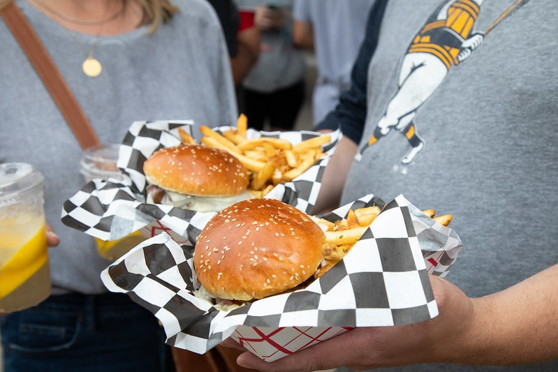 Two friends in West Allis, WI, happily holding burgers and fries in baskets, ready to enjoy their meal together.