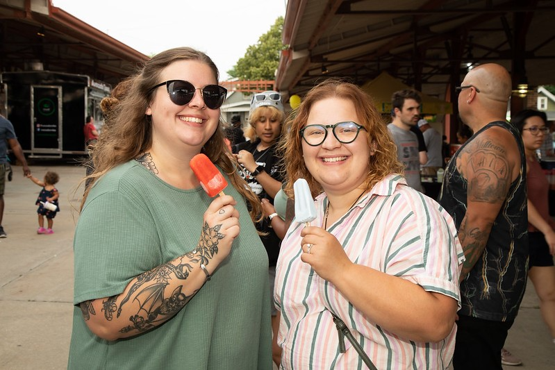 Two tattooed women in sunglasses enjoy ice cream together in West Allis, WI, radiating joy and summer vibes.