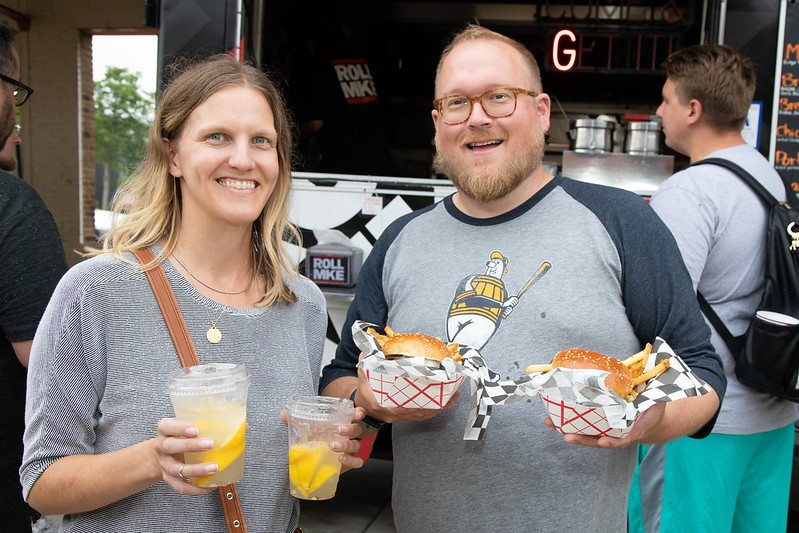 A man and woman happily holding delicious food from a vibrant food truck in West Allis, WI, enjoying their meal together.