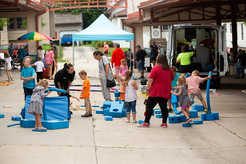  A joyful group of children splashes around with colorful water toys in a sunny West Allis parking lot.