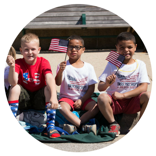 A cheerful group of kids sitting on a blanket, joyfully surrounded by American flags, celebrating together.