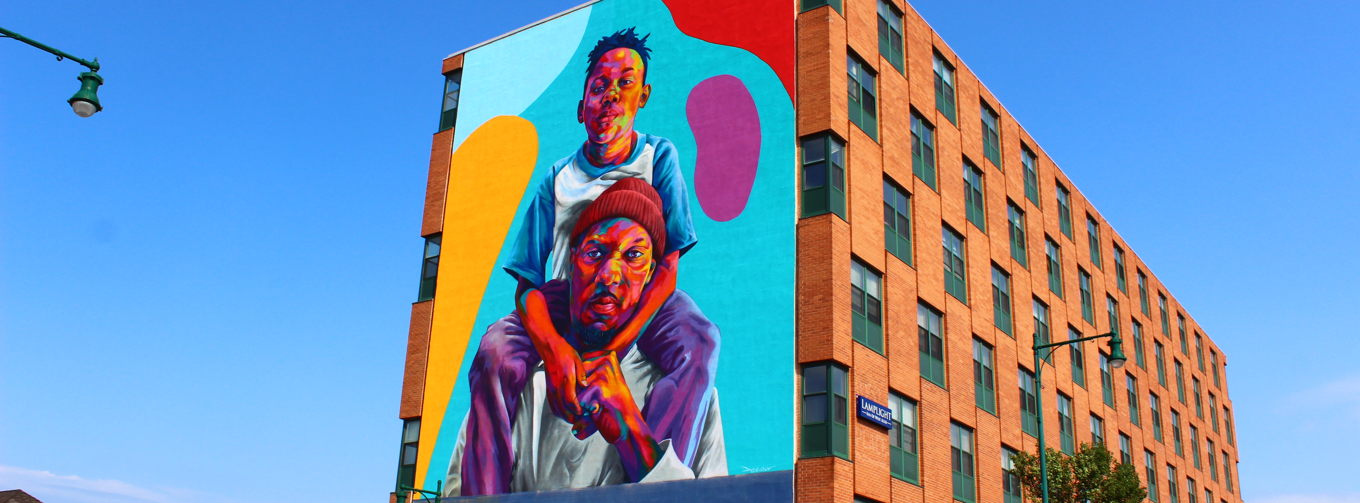 Photograph of mural by Thomas Detour Evans showing a proud Black father with his beautiful young son on his shoulders.