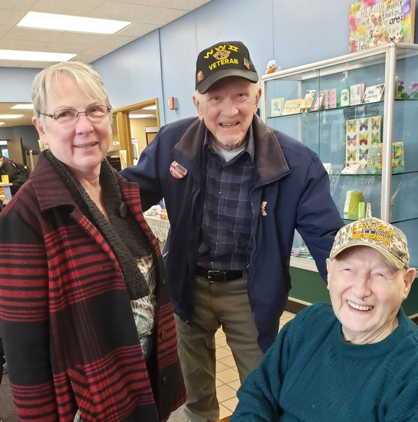 Three smiling individuals pose together in a store, showcasing the Milwaukee County Department of Aging Senior Meal Program.Three smiling individuals pose together in a store, showcasing the Milwaukee County Department of Aging Senior Meal Program.