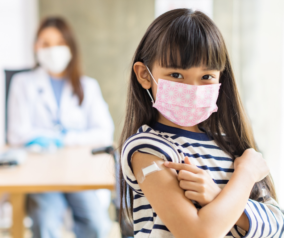 A little girl wearing a mask grips a syringe