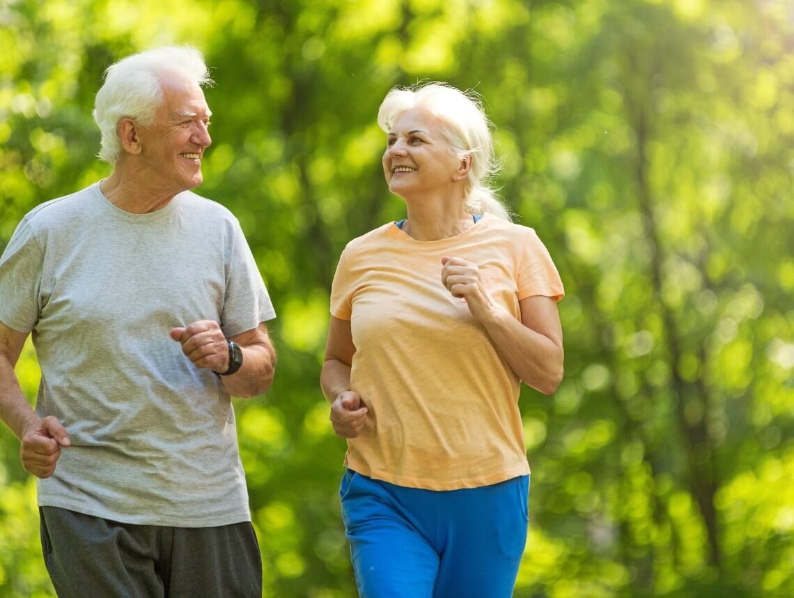 Senior couple jogging together in the park, promoting fitness and fall prevention through active lifestyle choices.