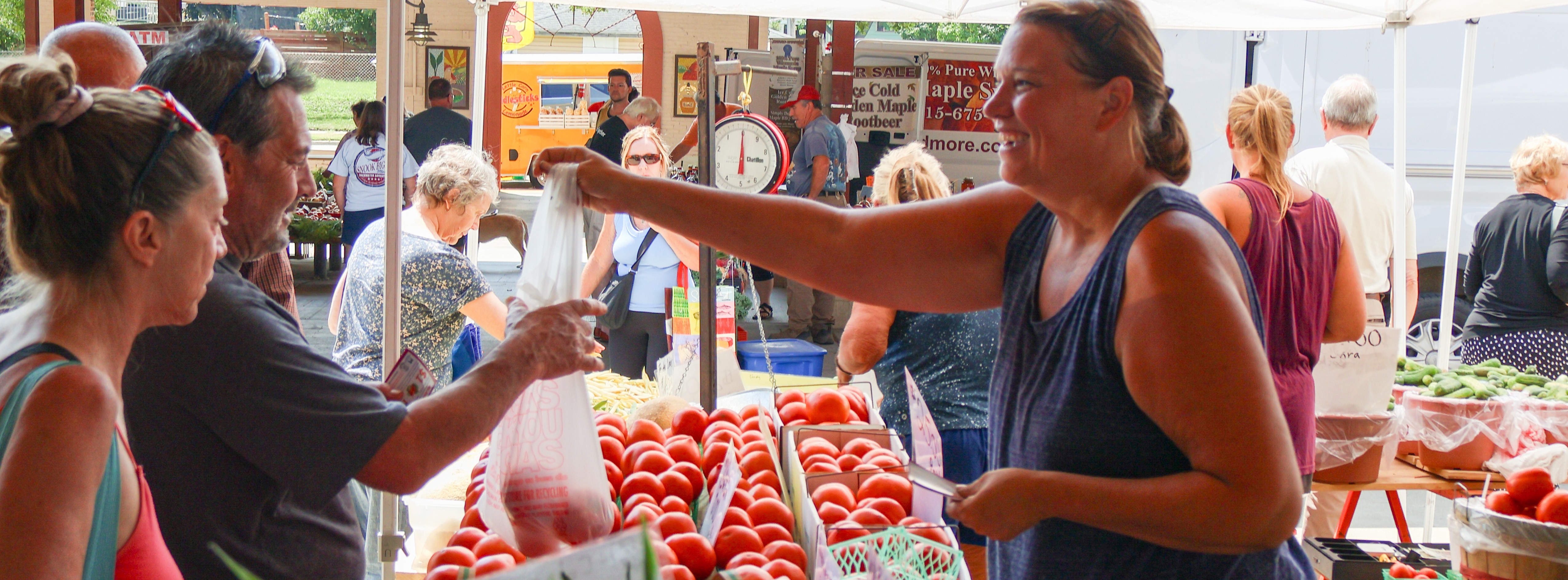 A farmers market vendor hands produce to a customer