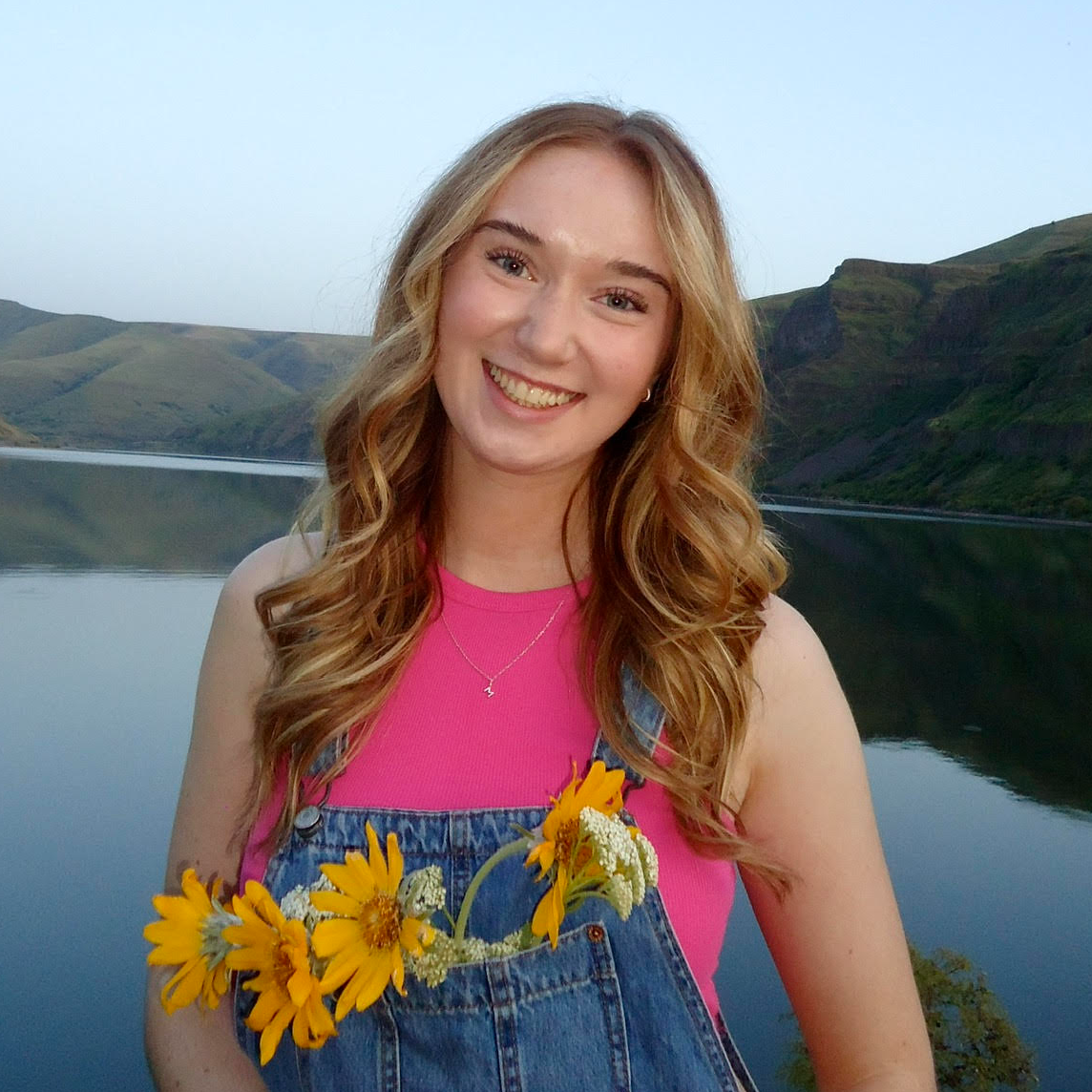 Photo of a staff member who is standing in front of a lake holding a bouquet of yellow sunflowers