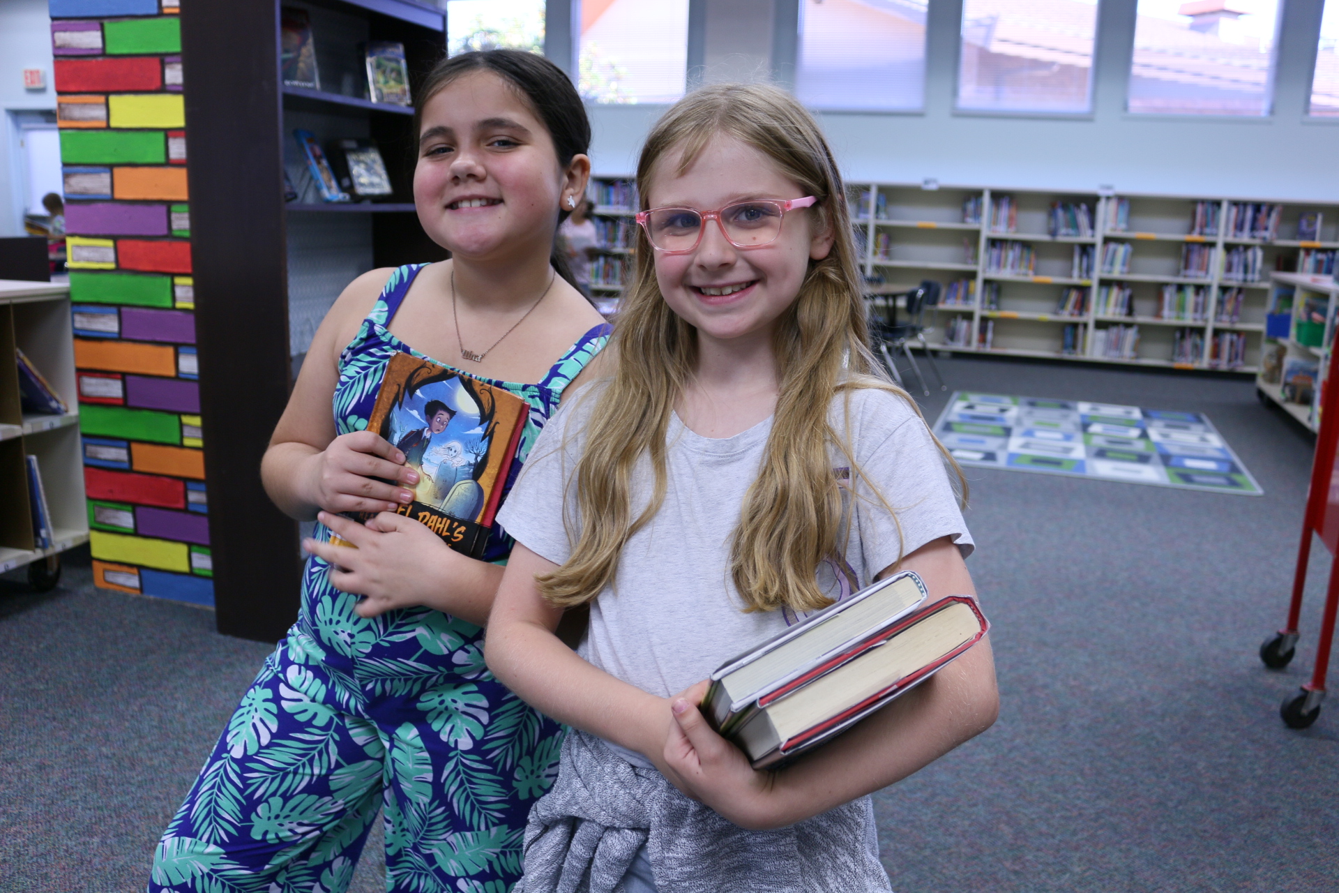Two girls hold library books and smile in the school library
