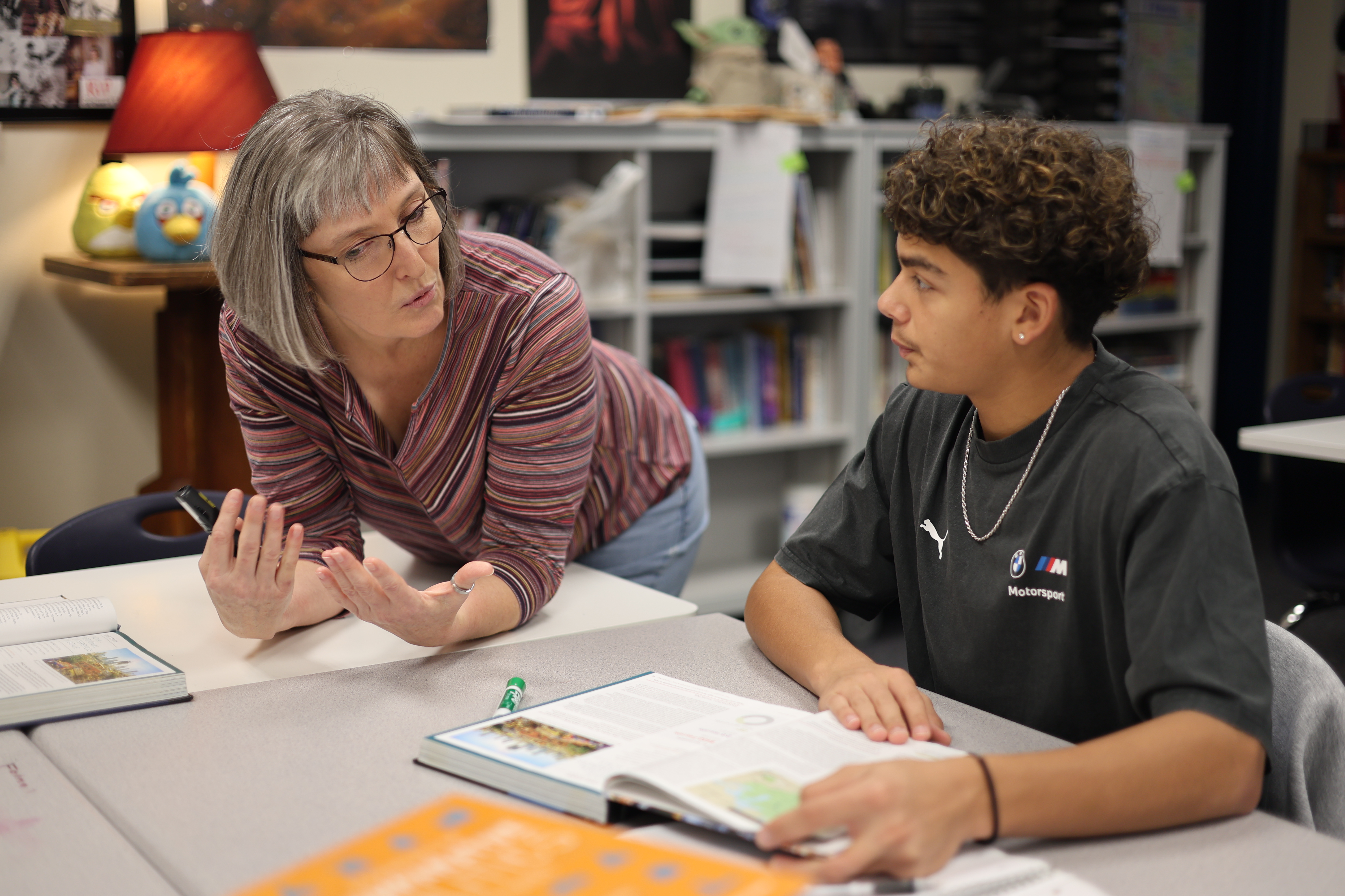 Teacher leans over desk to talk with high school student