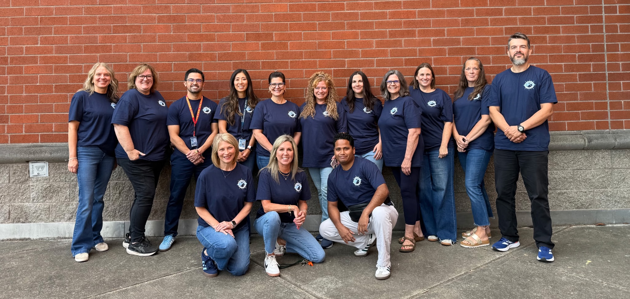 Group of staff members wearing spirit shirts in front of a brick school exterior wall