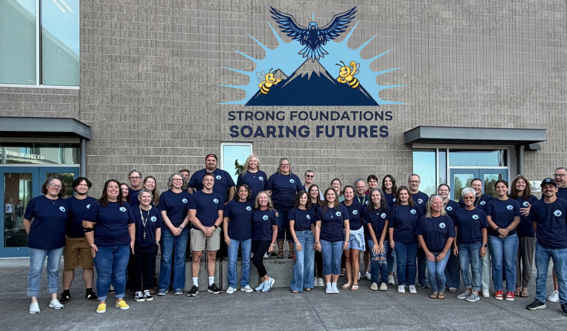 Group of staff members wearing spirit shirts in front of a school with text on the building that reads "Home of the Hornets"