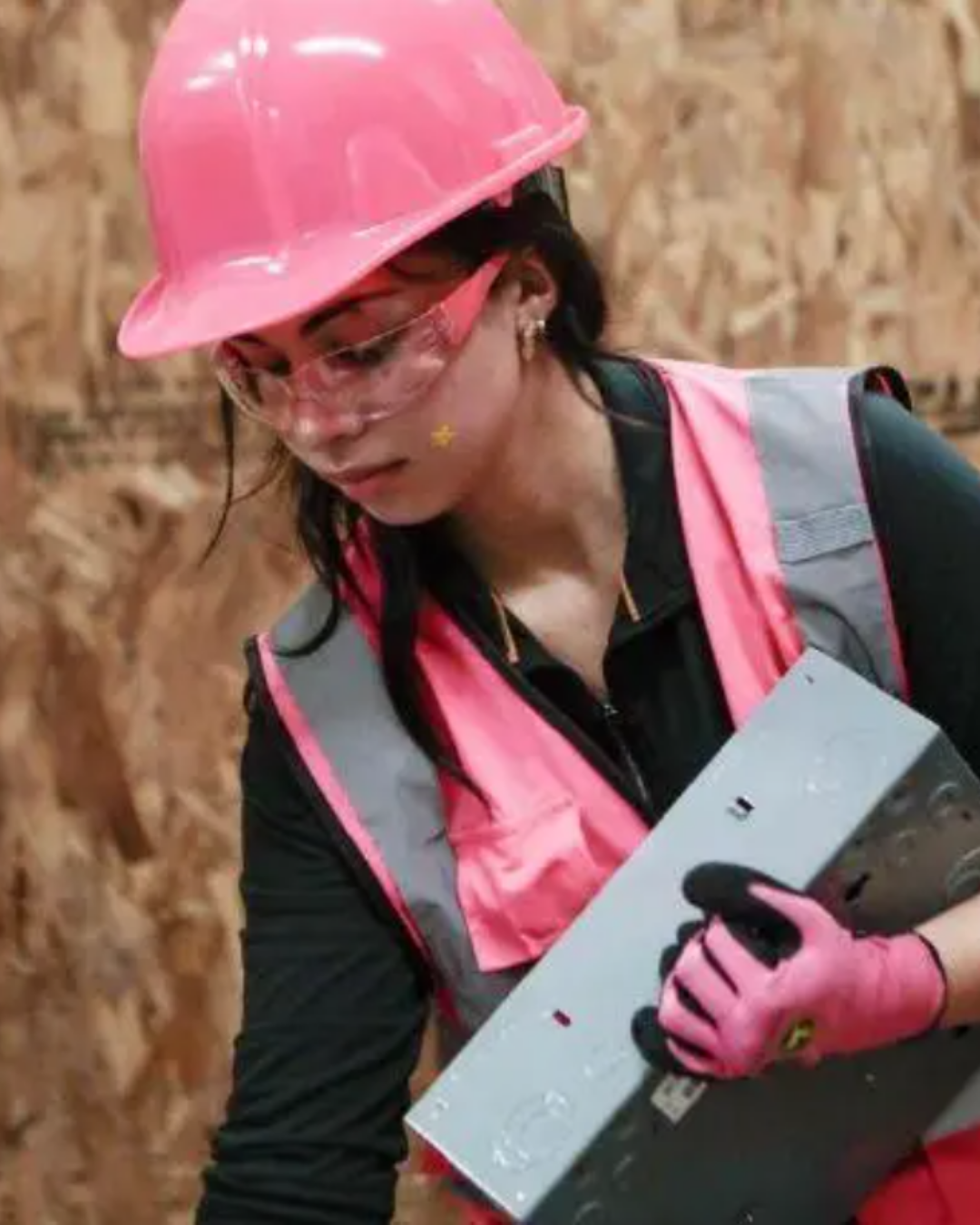 Student wears pink hard hat and works with wood