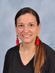 A woman with long brown hair, wearing a black top and red earrings, smiles against a light blue background.