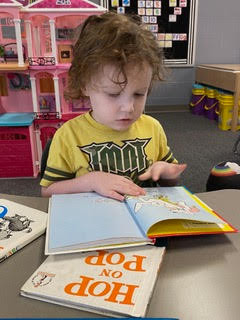 A young boy sitting at a desk in a classroom, focused on reading a book.