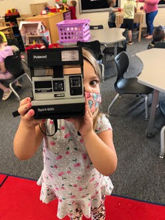 A young girl smiling while holding a Polaroid camera.