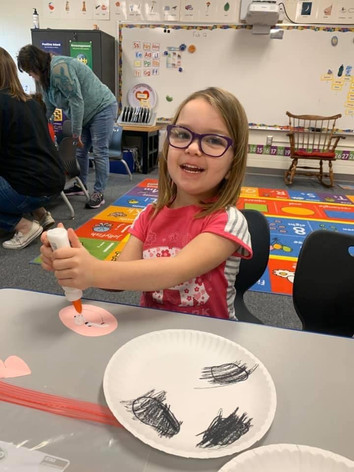 A young girl happily paints a paper plate using a black marker