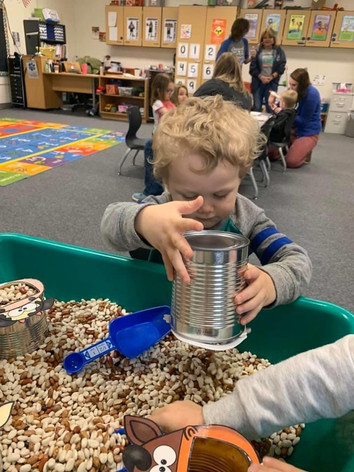 Child playing with tin can in preschool classroom.