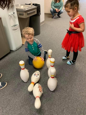 Two kids playing with bowling pins indoors.
