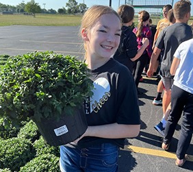 A girl holding a plant in a parking lot, smiling.