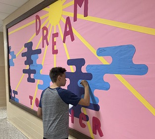 A young boy painting a colorful poster on a white wall.