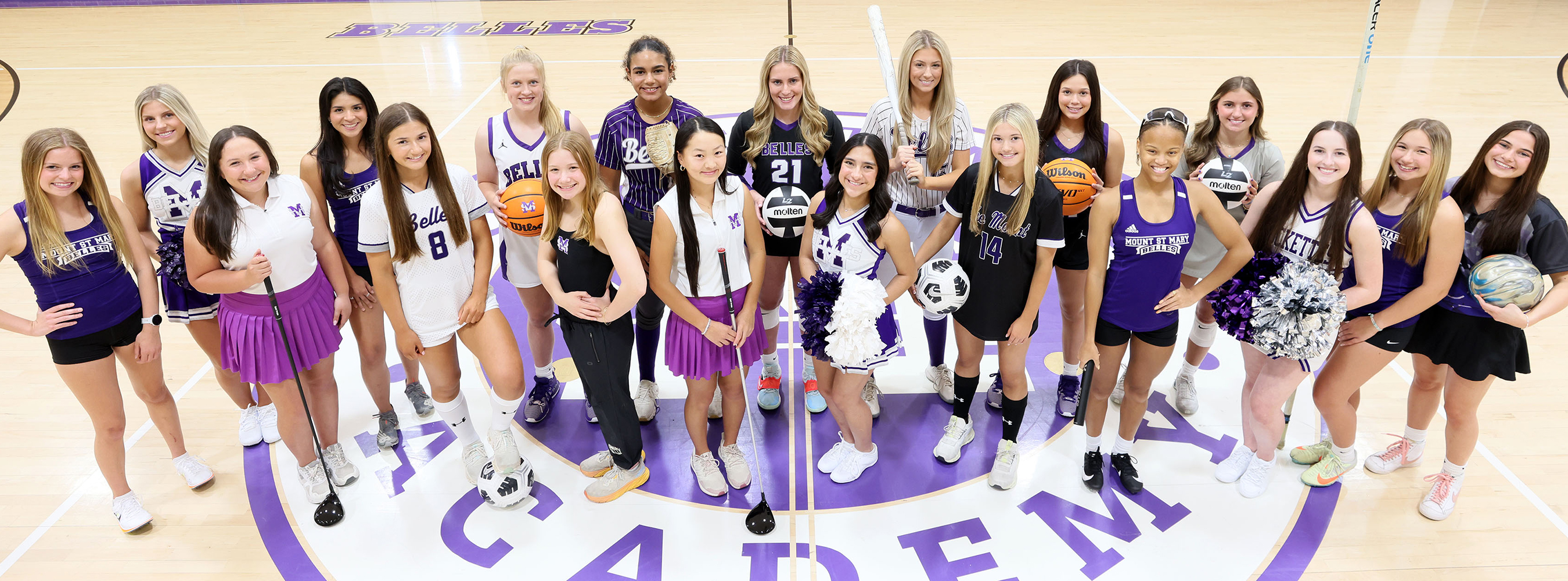 large group of student-athletes in uniform representing various sports and standing at center of basketball court