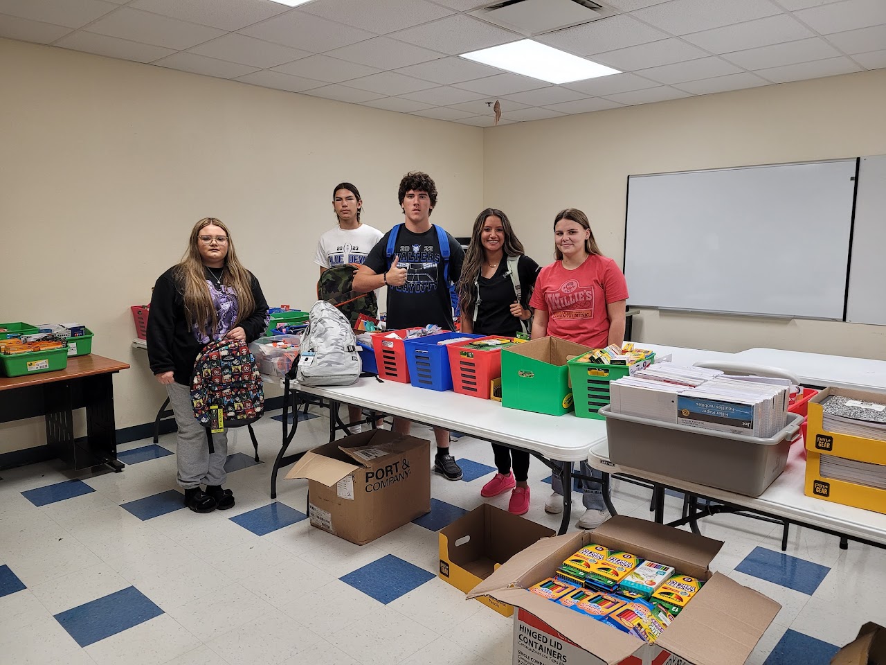 A diverse group of individuals gathers around a table filled with various supply boxes, engaged in discussion and planning.