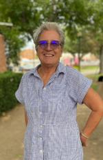 A woman wearing a blue dress and sunglasses stands confidently in front of a modern building, showcasing her stylish look.