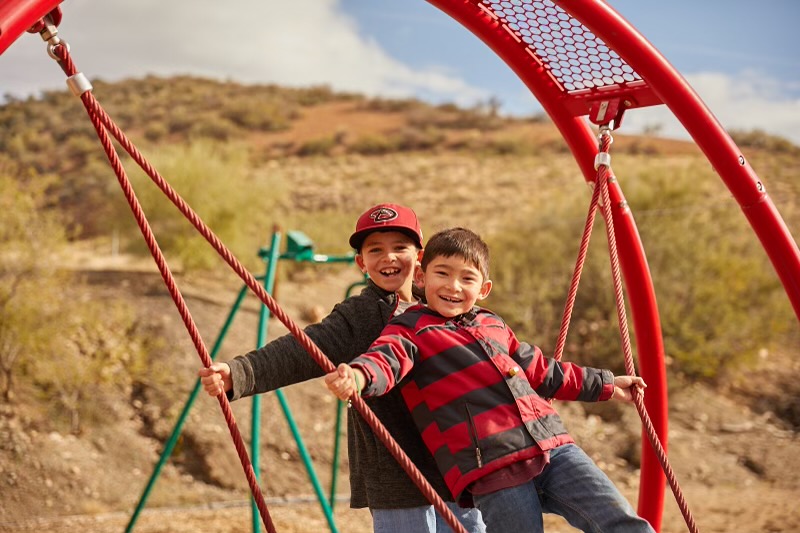 Two boys happily swinging at a playground.