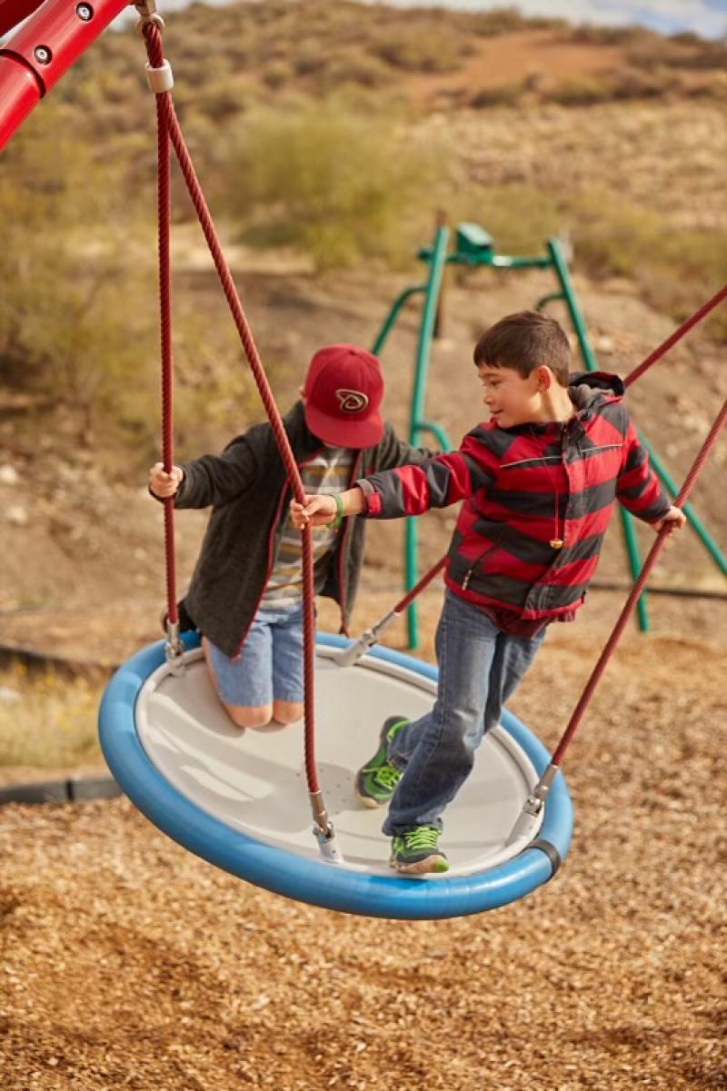 Two boys happily swinging on a swing set in a sunny playground, enjoying their time together.