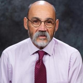 A bearded man in glasses wearing a purple shirt and red tie.
