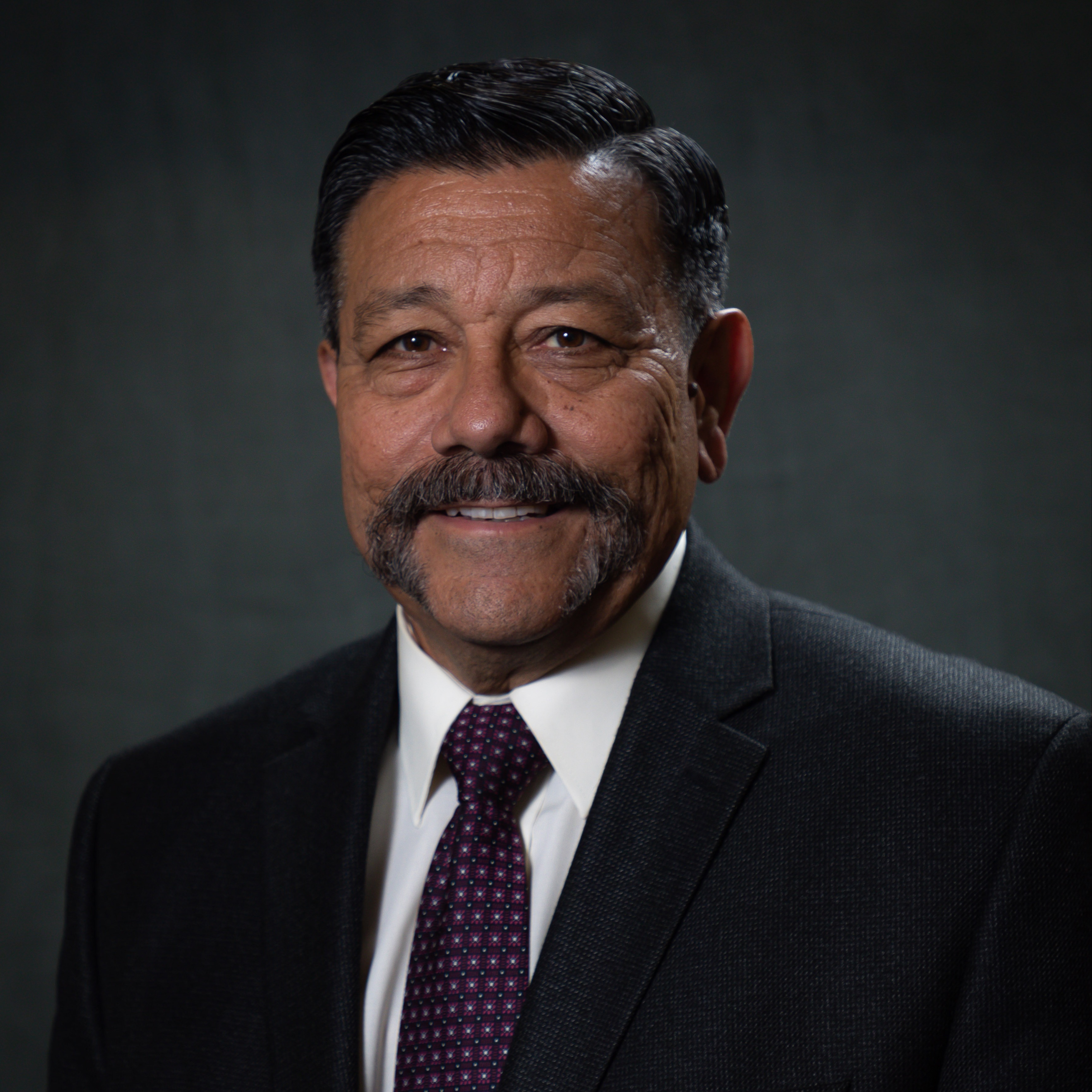 Mayor Al Gameros in a suit with a prominent mustache, exuding confidence and sophistication in a professional setting.