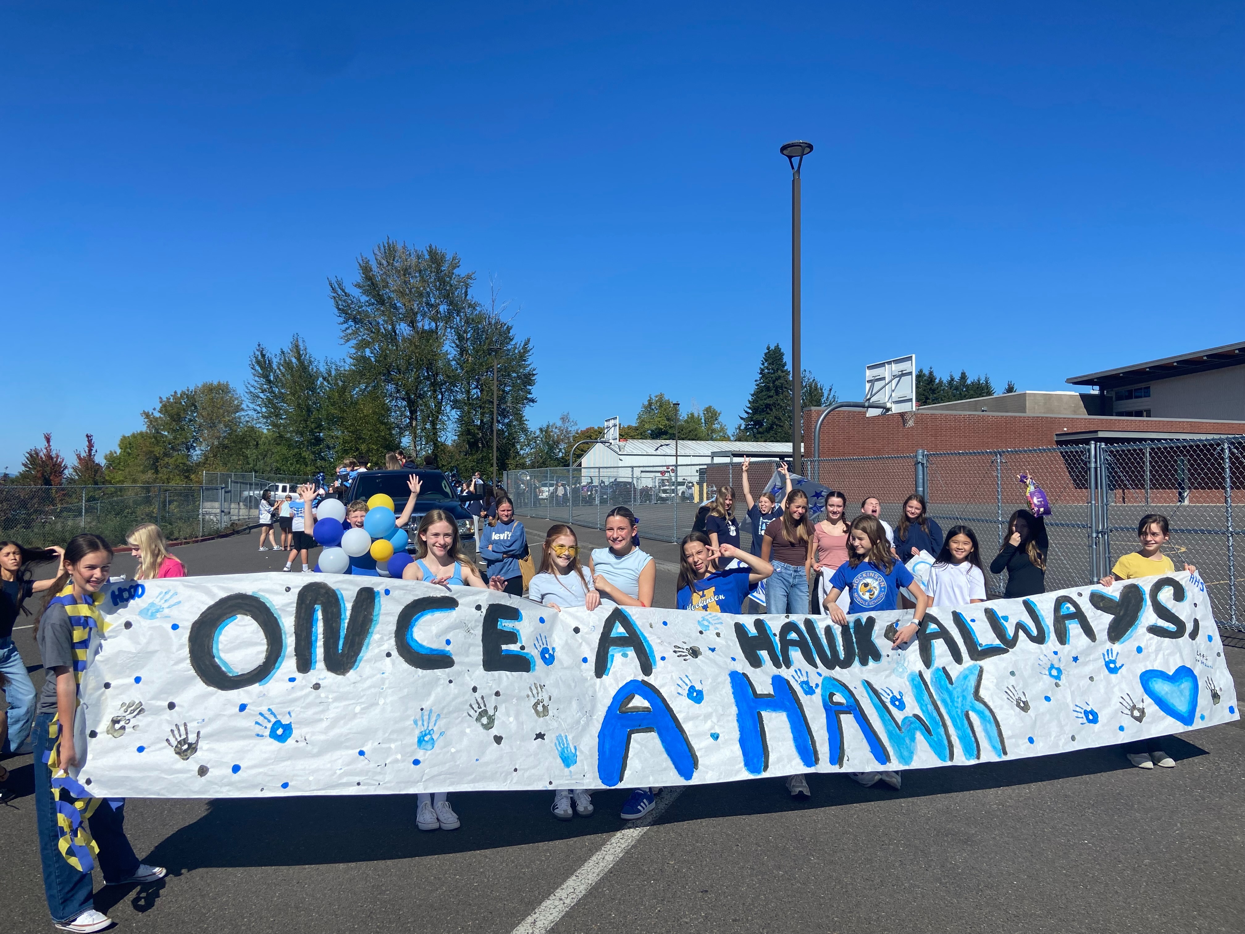 Group of students holding a giant banner that reads "Once a hawk always a hawk" outdoors