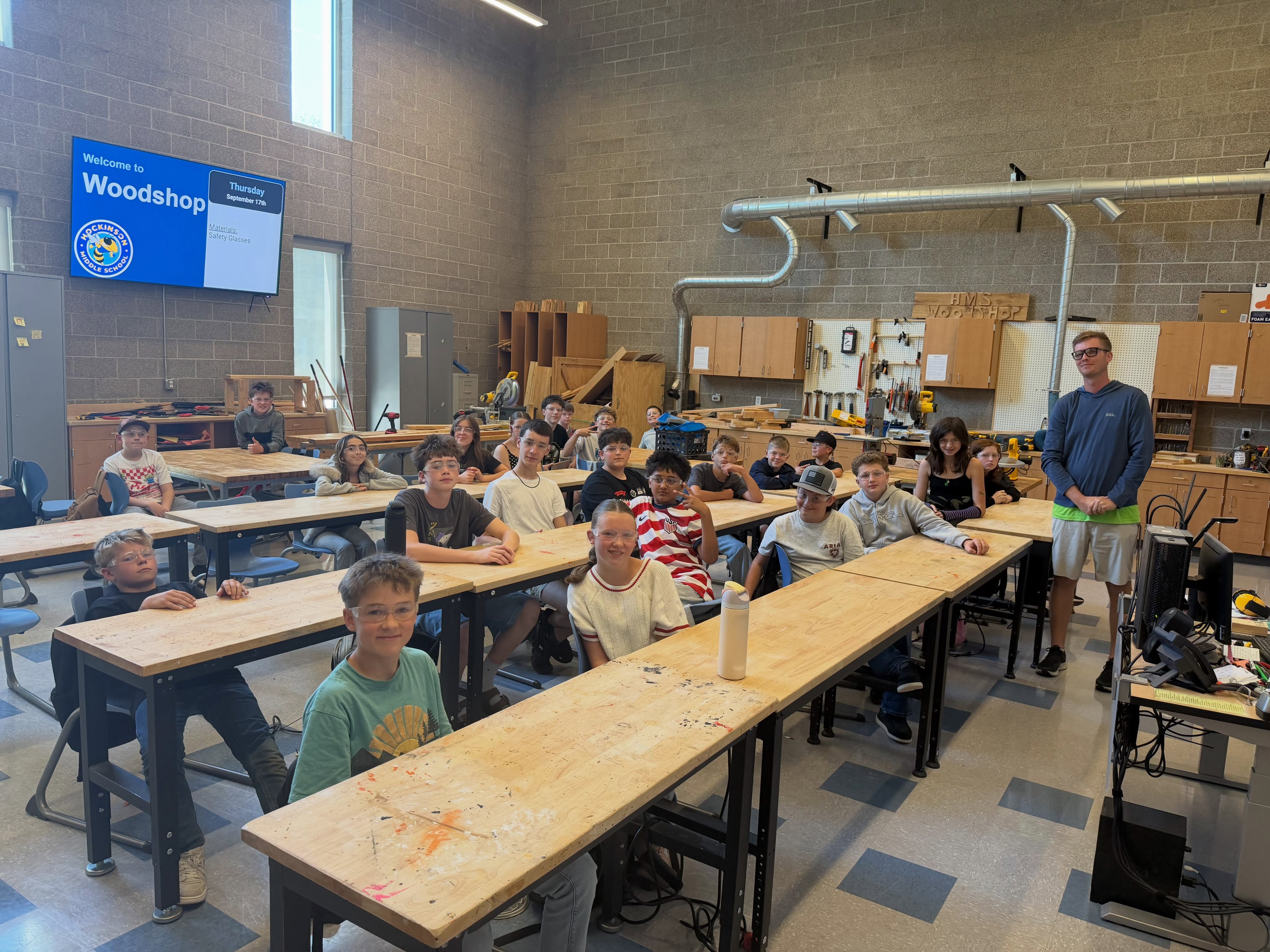 Woodshop class with goggles on sitting at desks.