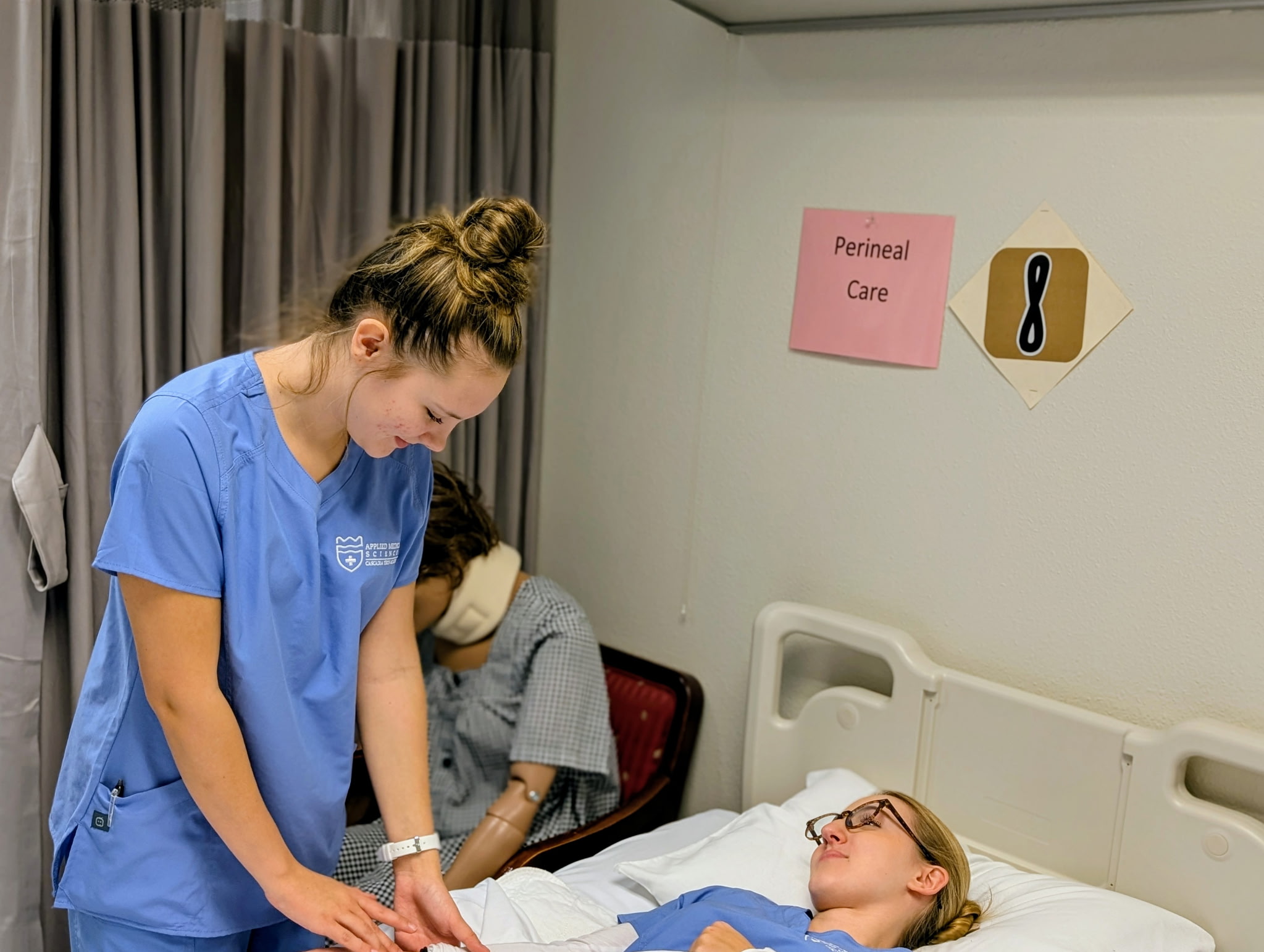 Student leans over a hospital bed to practice medical skills
