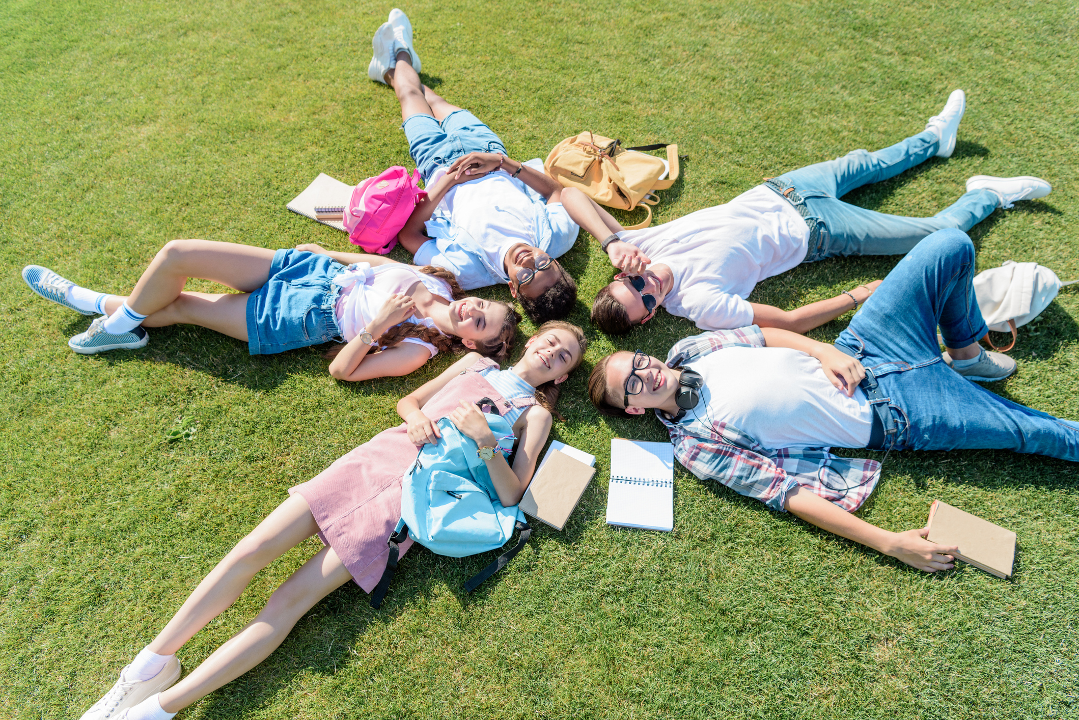 Group of students laying on their backs in the grass in a circle.