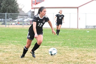 A girl in a black soccer uniform skillfully kicks a soccer ball on the field, showcasing her athleticism and focus.