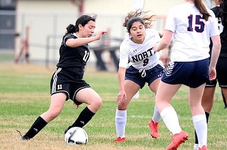 Three young female soccer players in uniforms competing in a game on the field.