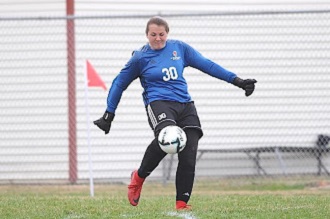 A female soccer player in blue and black uniform kicking a soccer ball.
