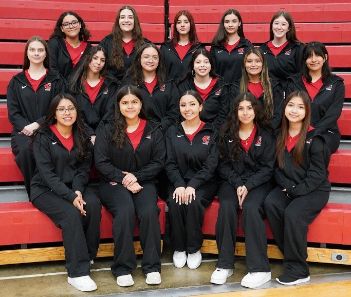 Group of female basketball players smiling and posing for team photo on court.