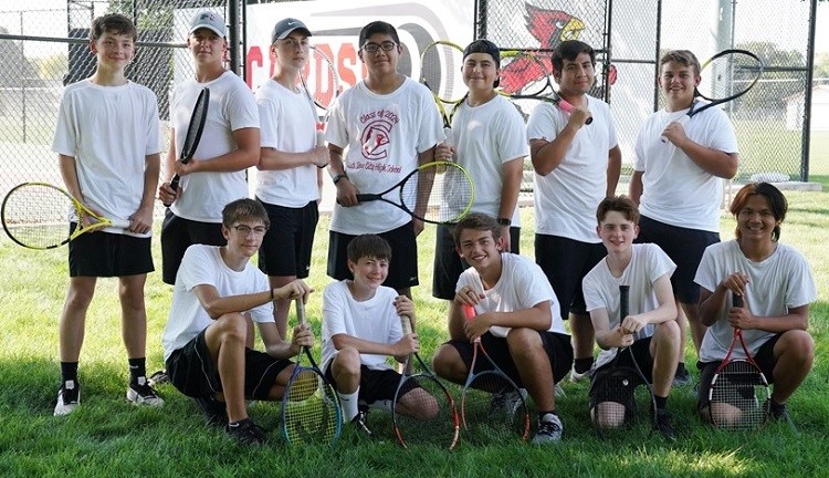 A group of young men smiling and posing together, each holding a tennis racket in a vibrant outdoor setting.